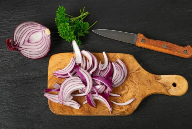 Une image montrant un oignon cru coupé en deux, placé à côté d'un couteau et d'une planche à découper, symbolisant les avantages et inconvénients de manger un oignon cru le soir