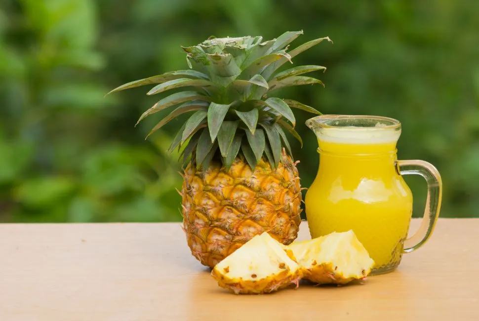 Image illustrant un verre de jus d'ananas frais, à côté de tranches d'ananas, évoquant le thème de l'utilisation du jus d'ananas dans la récupération post-opératoire des dents de sagesse